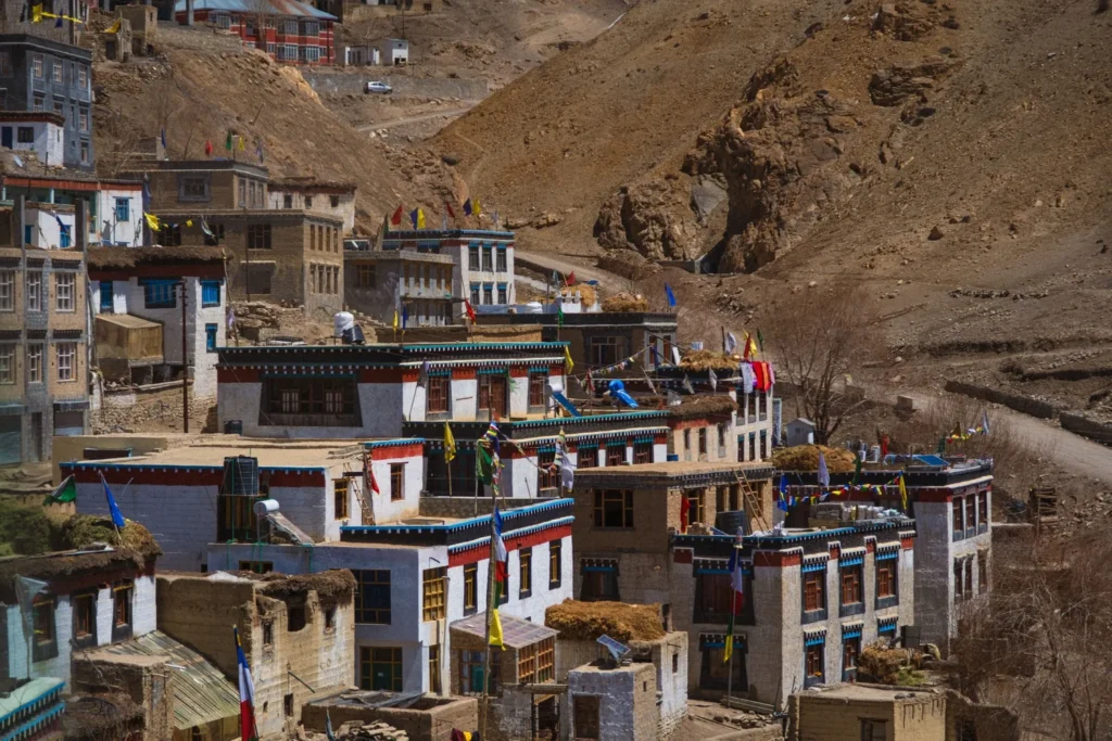 Village buildings with colourful flags against dry mountain slopes.