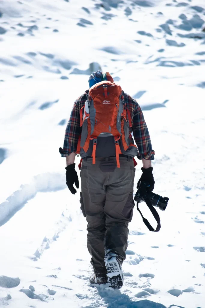 Person carrying a camera across a snow-covered mountain landscape.